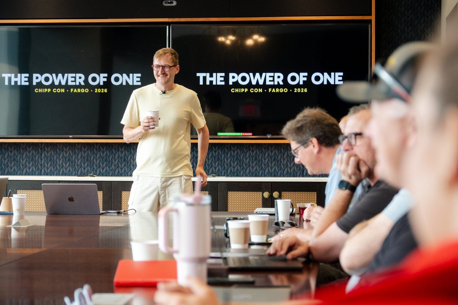 A Chipp Con speaker smiles at the room in front of a The Power of One slide